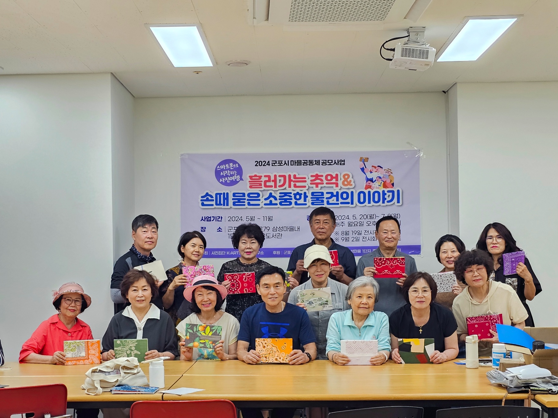 2024 군포시 마을공동체 공모사업 배너 앞에서 수강생들이 완성된 책을 들고 환하게 웃는 단체 사진